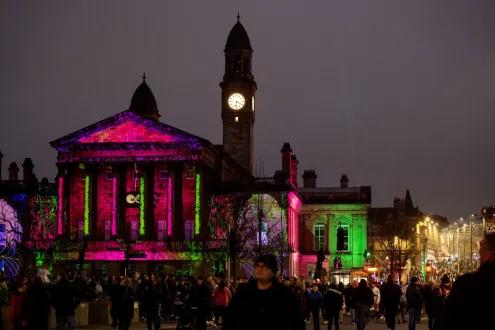 Crowds at Paisley Halloween Parade in front of a lit-up historic building with spooky projections.