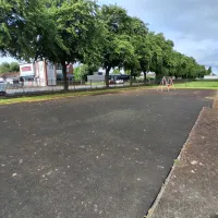 A tarmac area with nothing on it, on the edge of an area of grass.