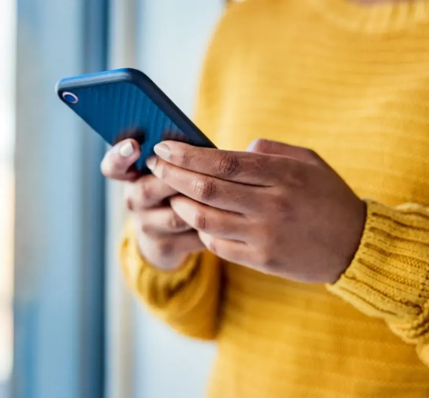 Person wearing a bright yellow jumper and holding a mobile phone.