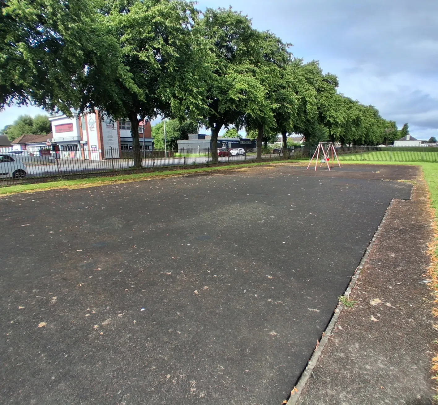 A tarmac area with nothing on it, on the edge of an area of grass.