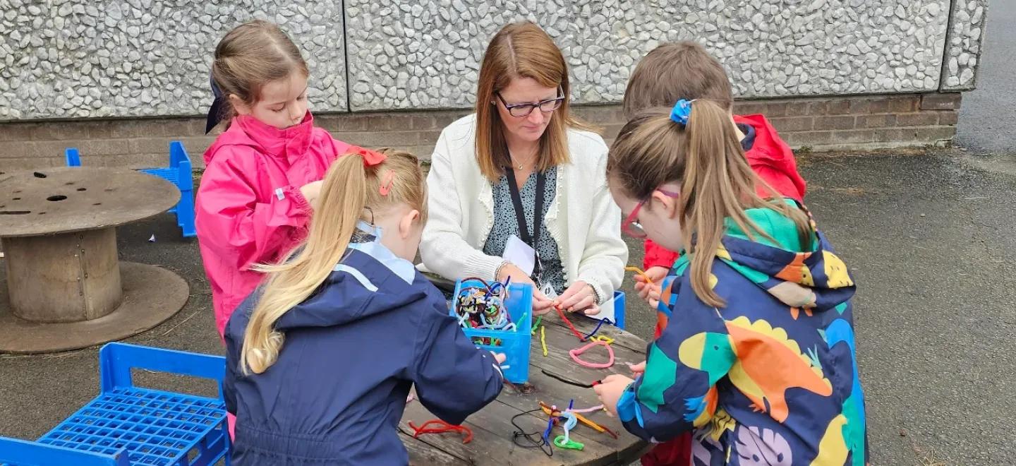 A teacher and four pupils use pipe cleaners for STEM learning.