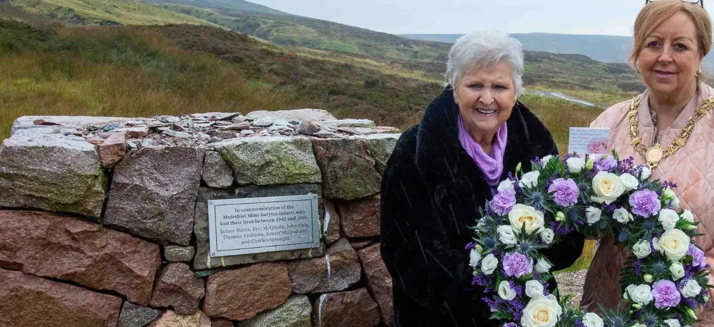 Mrs Burns and Provost Cameron holding a wreath at a memorial cairn