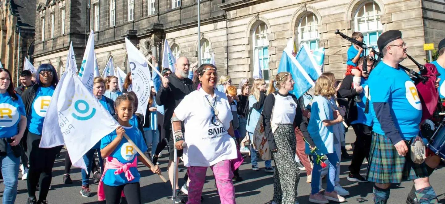A crowd of people march with banners through Paisley for the 2022 Recovery Walk.