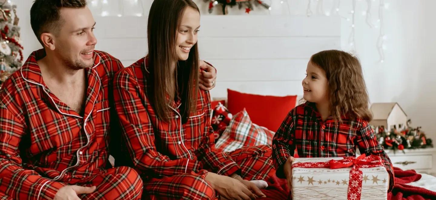 Two adults and a child wearing pyjamas opening Christmas gifts.