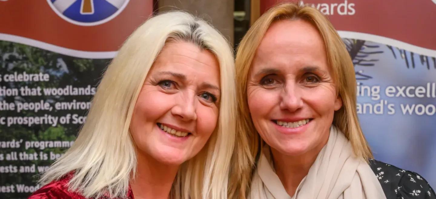 Rona Murray and Elaine Stevenson of West Johnstone Early Learning and Childcare Centre in front of display stands for Scotland's Finest Woods Awards.