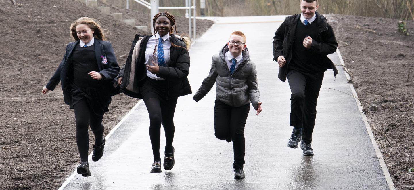 Two boys and two girls from Paisley Grammar running along a tarmacked road called the Gallowhilll Link. They are about to enter an underpass