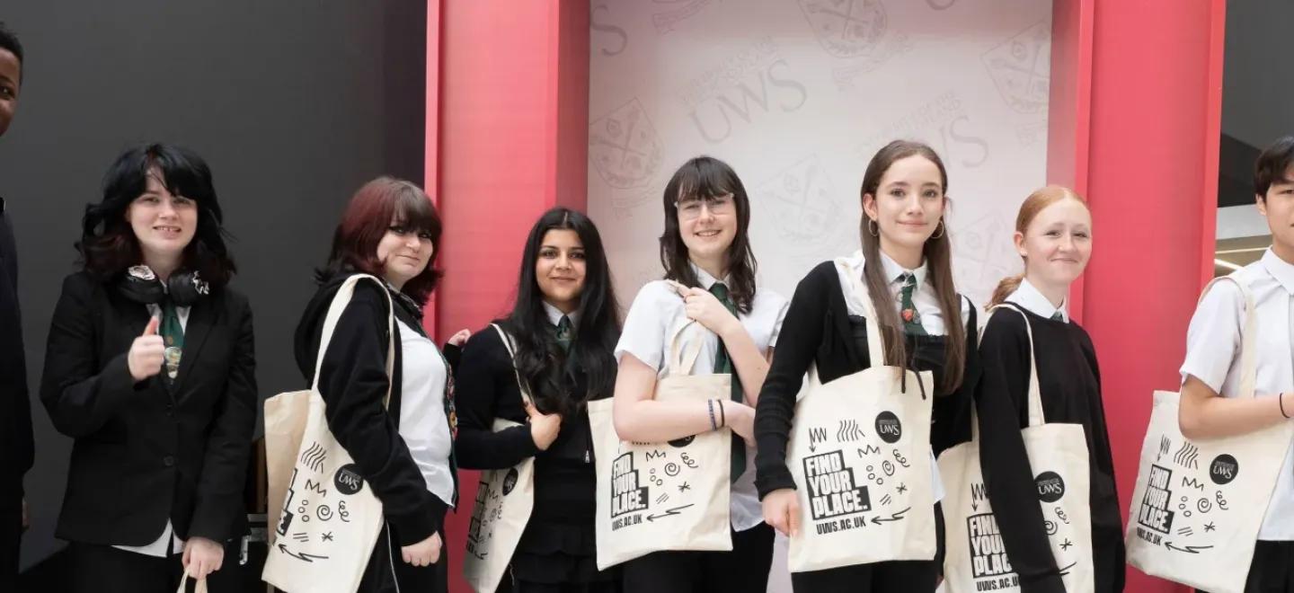 A group of third year pupils stand together holding tote bags from University of the West of Scotland.