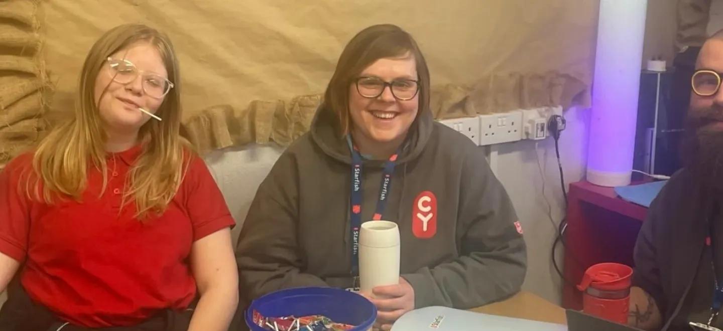 Two adults and a pupil smile while sitting at a table in a wellbeing room.