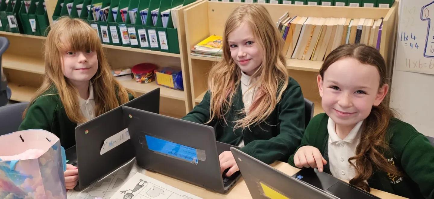 Three pupils use laptops in their classroom.
