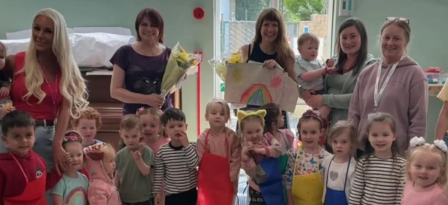 Children and nursery staff stand together in a room used for art.