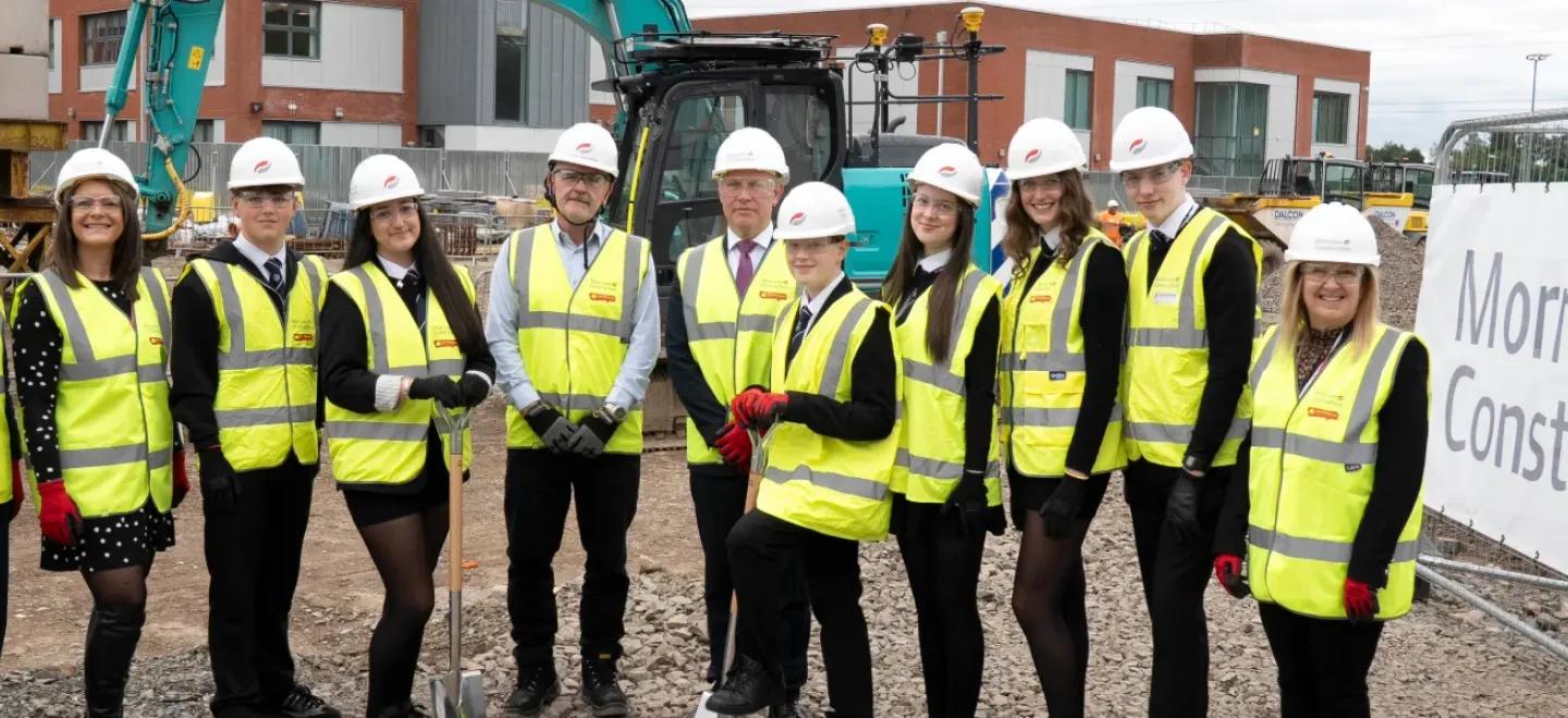 Young people and adults wear safety gear on site of construction site.