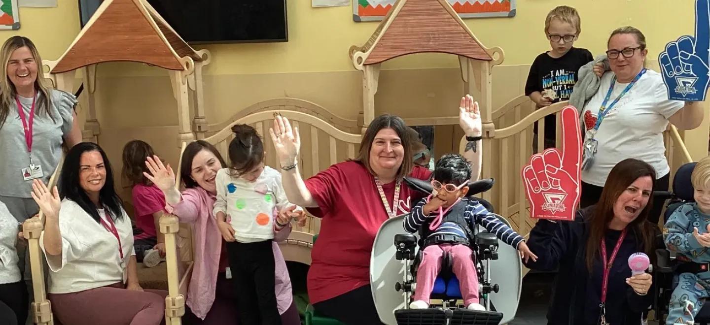 Nursery staff and children hold their hands in the air in celebration.