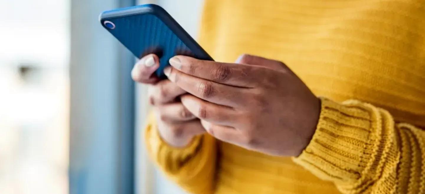 Person wearing a bright yellow jumper and holding a mobile phone.